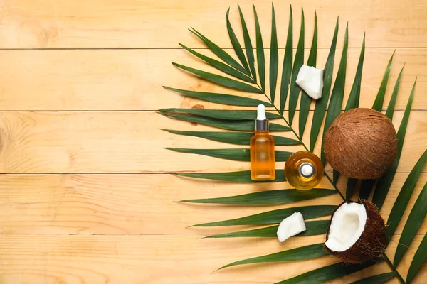Bej ahşap arka planda palmiye yaprağı olan hindistan cevizi kozmetik yağı şişeleri.