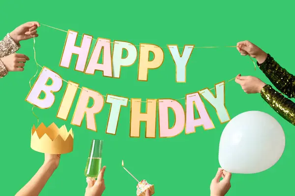 Female hands with birthday garland, champagne and cake on green background