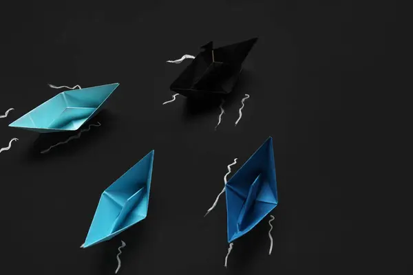 Colorful origami boats and drawn waves on black chalkboard