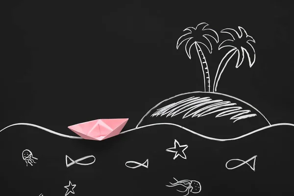 Pink origami boat and drawn island with sea creatures on black chalkboard