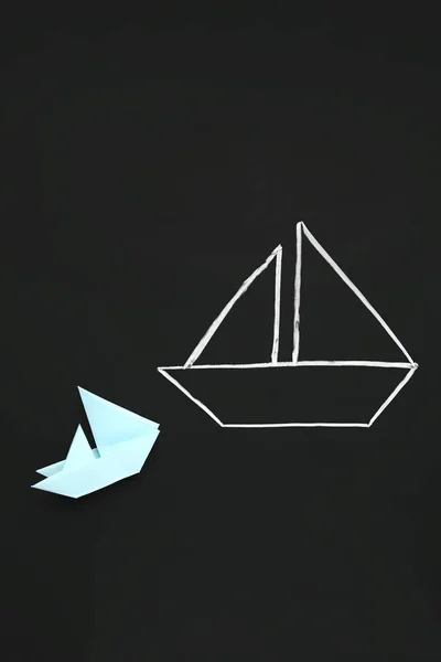 Drawn and colorful paper boats on black chalkboard