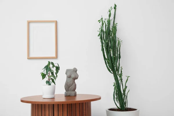 Big cactus with table and home decor near white wall in room