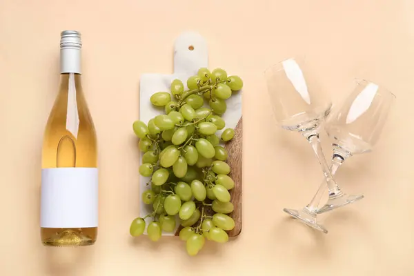 Wooden board with grapes and bottle of wine with blank label on color background