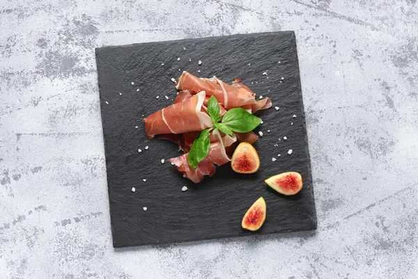 Gri arka planda lezzetli prosciutto dilimleri olan tahta