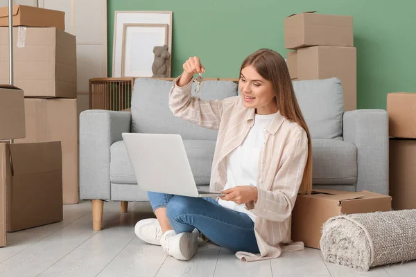 Yeni dairede dizüstü bilgisayarı ve anahtarlarıyla yerde oturan genç bir kadın. Taşınma konsepti