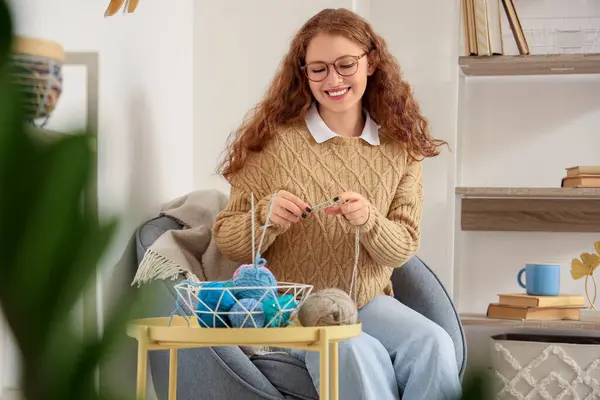 Evde iğnelerle örgü ören genç bir kadın.