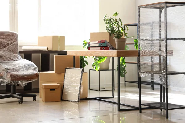 Interior of office with chair wrapped in stretch film and cardboard boxes on moving day