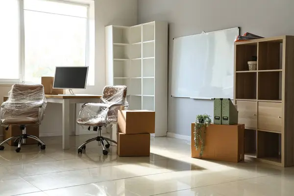 Interior of office with chairs wrapped in stretch film and cardboard boxes on moving day