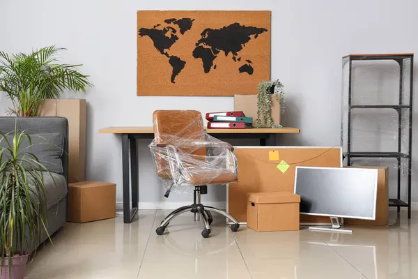 Interior of office with chair wrapped in stretch film and cardboard boxes on moving day