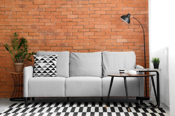 Kahverengi tuğla duvarın yanında rahat gri kanepesi ve sehpası olan modern oturma odasının içinde.