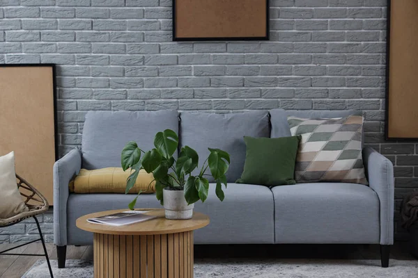 Interior of modern living room with cozy grey sofa and coffee table near brick wall