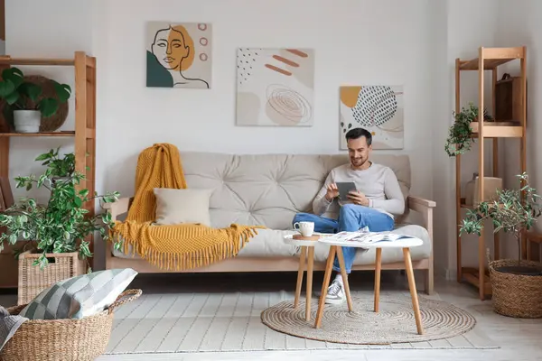 Modern oturma odasındaki beyaz koltukta dinlenen tablet bilgisayarlı yakışıklı adam.