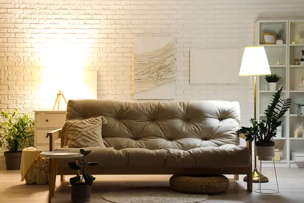 Interior of modern living room with white sofa and glowing lamps at evening