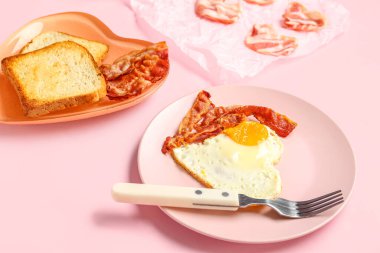 Lezzetli pastırmalı tabaklar, kızarmış yumurtadan yapılmış kalp ve pembe arka planda tost, yakın plan.