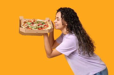 Sarı arka planda lezzetli pizzası olan güzel, mutlu, Afro-Amerikalı bir kadın.