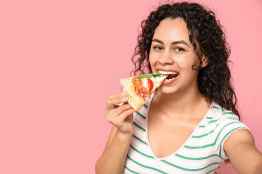 Güzel, mutlu, Afro-Amerikan bir kadın lezzetli pizzalar yiyor pembe arka planda selfie çekiyor.