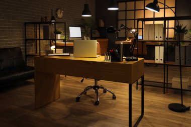 İşyeri, raf üniteleri ve geceleri parlayan lambalar olan karanlık ofisin içinde.