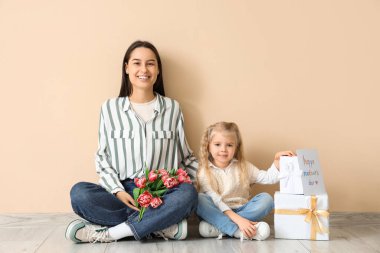 Küçük kız, mutlu annesini bir buket çiçek, tebrik kartı ve bej duvarın yanındaki hediye kutularıyla tebrik ediyor. Anneler Günü kutlaması