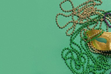 Mardi Gras kutlamaları için yeşil arka planda karnaval maskeli renkli boncuklar.