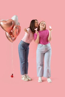 Pembe arka planda kağıt kalpleri ve balonları olan genç lezbiyen çift. Sevgililer Günü kutlaması