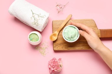 Kadın eli, bir kase vücut fırçası, deniz tuzu ve pembe arka planda temiz havlu, yakın plan.