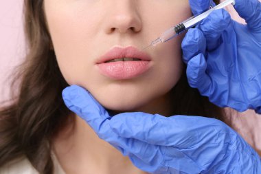 Güzel bir kadın pembe arka planda dudak enjeksiyonu yaptırıyor.