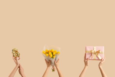 Sarı lale buketli kadın eller, şekil 8 şeklinde balon ve bej arka planda hediye kutusu. Uluslararası Kadınlar Günü kutlamaları