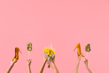 Şekil 8 şeklinde balonları olan kadın eller, pembe arka planda sarı laleler ve yüksek topuklu ayakkabılar. Uluslararası Kadınlar Günü kutlamaları