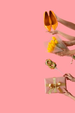 Hediye kutusu olan kadın eller, sarı laleler ve pembe arka planda yüksek topuklu ayakkabılar. Uluslararası Kadınlar Günü kutlamaları
