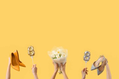 Şekil 8 şeklinde balonları olan kadın eller, yüksek topuklu ayakkabılar ve sarı arka planda bir buket lale. Uluslararası Kadınlar Günü kutlamaları