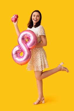8 numaralı figür şeklinde pembe hava balonu ve sarı arka planda hediye kutusu olan mutlu genç bir kadın. Uluslararası Kadınlar Günü