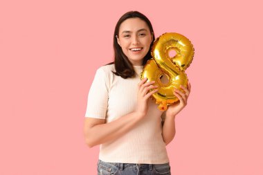 Pembe arka planda 8 numaralı figür şeklinde altın renkli hava balonu olan güzel genç bir kadın. Uluslararası Kadınlar Günü
