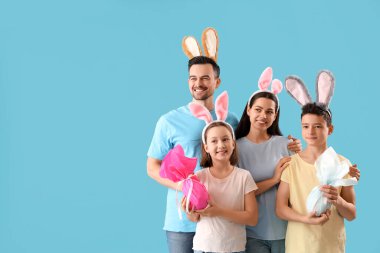 Mavi arka planda Paskalya hediyesi yumurtaları olan tavşan kulaklı mutlu bir aile.
