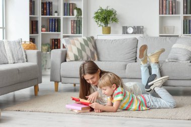 Küçük çocuk ve annesi evde yerde yatarken kitap okuyorlar.