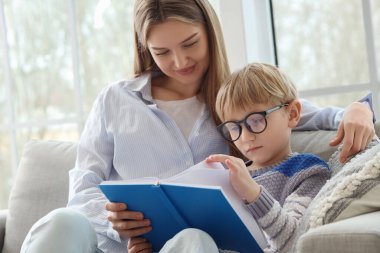 Anne ve oğlu evde kitap okuyorlar.