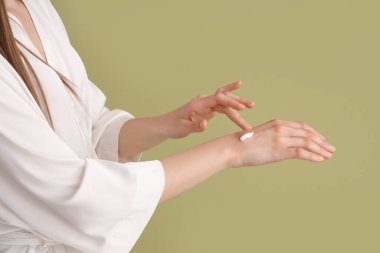 Yeşil arka planda krem süren kadın, yakın plan.