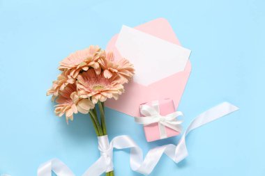 İçinde boş kart, hediye kutusu ve mavi arka planda Gerbera çiçekleri olan zarf.