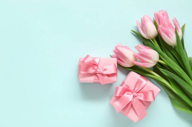 Mavi arka planda hediye kutuları olan pembe laleler.