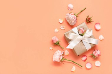 Turuncu arka planda gül ve taç yaprakları olan bir hediye kutusu.