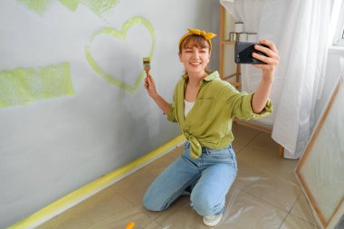 Kalbi çizilmiş genç bir kadın odada onarım sırasında selfie çekiyor.