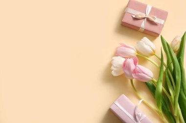 Bej arka planda Anneler Günü kutlamaları için hediye kutuları ve lale çiçekleri olan kompozisyon