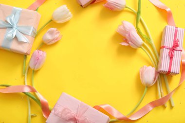 Sarı arka planda Anneler Günü kutlaması için hediye kutuları ve lale çiçeklerinden yapılmış çerçeve.