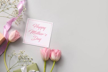 Mutlu Anneler Günü yazılı kart, hediye kutusu ve arka planda güzel çiçekler.