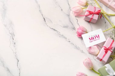 Mutlu Anneler Günü yazılı kart, hediye kutuları ve arka planda güzel çiçekler