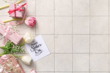 Mutlu Anneler Günü yazılı kart, hediye kutuları ve arka planda güzel çiçekler