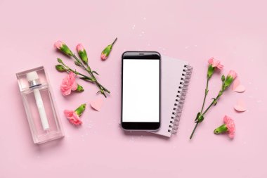 Modern cep telefonlu kompozisyon, bir şişe parfüm ve pembe arka planda karanfil çiçekleri.