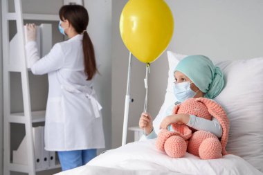 Oyuncak ve mavi balonla kemoterapiden sonra klinikte yatan küçük kız. Uluslararası Çocukluk Kanser Günü