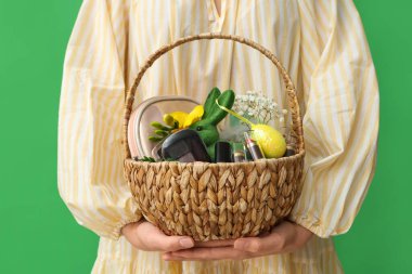 Yeşil arka planda kozmetik ürünleri olan Paskalya sepeti tutan genç bir kadın. Yakın plan.