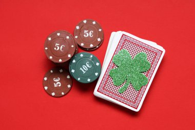 Poker fişleri, bir deste kağıt ve kırmızı arka planda şanslı yonca. Aziz Patrick Günü kutlaması