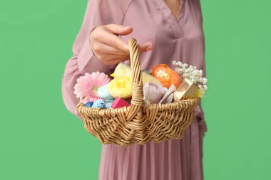 Yeşil arka planda kozmetik ürünleri olan hasır Paskalya sepeti tutan genç bir kadın.